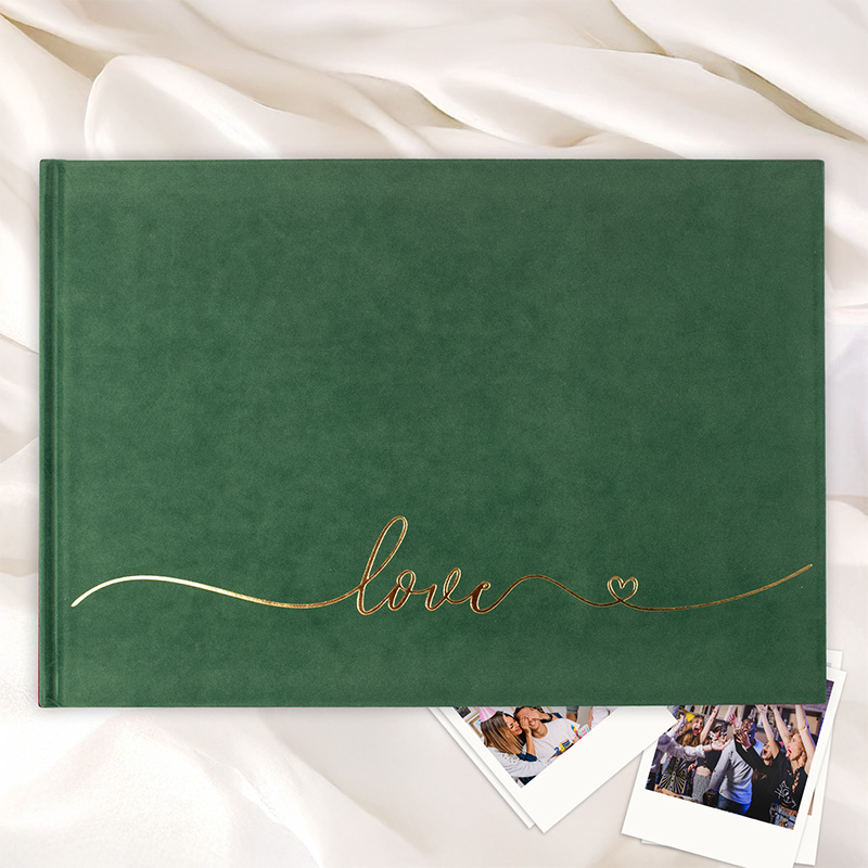 Zielony album fotograficzny na tle białego materiału, z napisem 'love' w złotej, eleganckiej czcionce oraz małym sercem, otoczony zdjęciami leżącymi na stole.