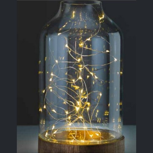 Szkło z ozdobnymi światełkami LED w szklanym pojemniku, stojącym na drewnianej podstawie, na ciemnym tle.