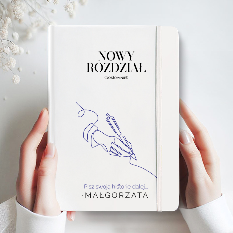 Osoba trzymająca biały notes z napisem 'NOWY ROZDZIAŁ (DOSŁOWNIE!)' oraz ilustracją ręki trzymającej pióro. U dołu znajduje się tekst 'Pisz swoją historię dalej... Małgorzata'. Tło jest jasne z delikatnymi kwiatami po lewej stronie.