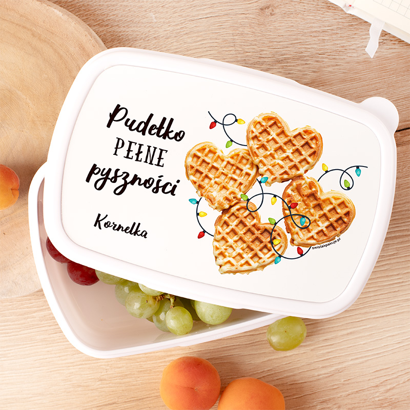 Biała pojemnik z napisem "Pudełko PEŁNE pyszności" oraz grafiką przedstawiającą wafle w kształcie serca z kolorowymi lampkami, na drewnianym tle z owocami w środku.