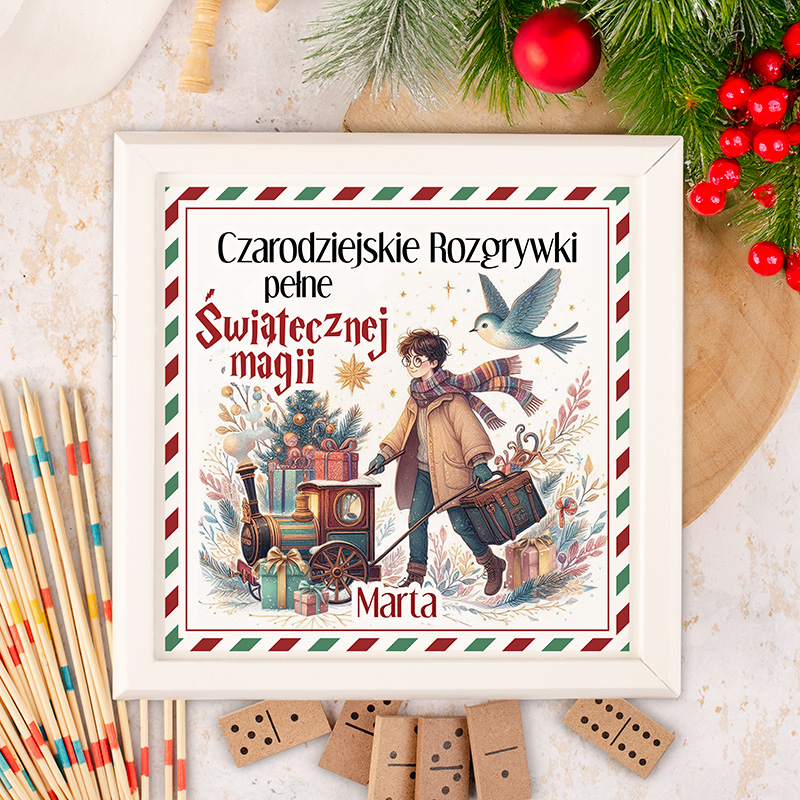 Ilustracja okładki książki z tytułem 'Czarodziejskie Rozgrywki pełne Świątecznej magii', przedstawiająca postać chłopca z walizką i wózkiem, wypełnionym prezentami, obok choinki, z ptakiem w locie w tle, na ozdobnym tle w kolorach świątecznych.