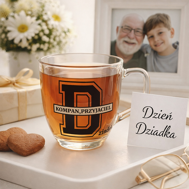 Szklanka z herbatą z napisem "KOMPAN, PRZYJACIEL" obok kartki z życzeniami "Dzień Dziadka" i ciasteczkami na stole.