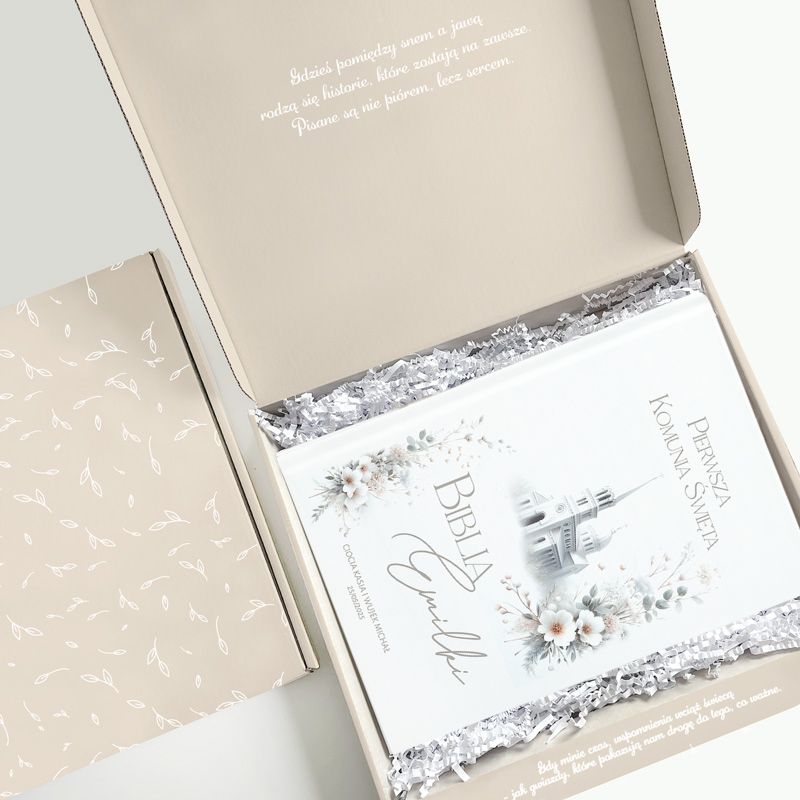 Otwarte pudełko z Biblią, na której okładce znajdują się kwiaty i świątynia; w środku białe wypełnienie.
