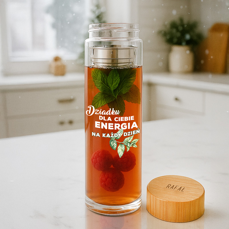 Szklany dzbanek z herbatą zawierający świeże liście mięty i maliny, z napisem 'Dziadku dla Ciebie energia na każdy dzień' na przezroczystej ściance; obok znajduje się drewniana nakrętka z napisem 'RAFAŁ'.