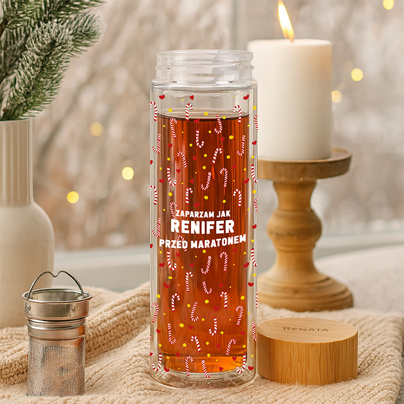 Przezroczysty słój z napojem, ozdobiony wzorami cukierków, w drugim planie świeca i drewniane akcesoria, w tle ozdobne światła.