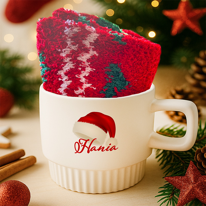 Kremowa filiżanka z kolorowym nadrukiem czapki mikołaja w zestawie ze skarpetami.