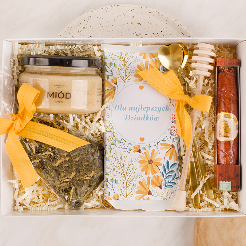 Zestaw prezentowy zawierający miód, herbatę, świeczkę, złote łyżeczki oraz opakowanie z napisem "Dla najlepszych Dziadków".