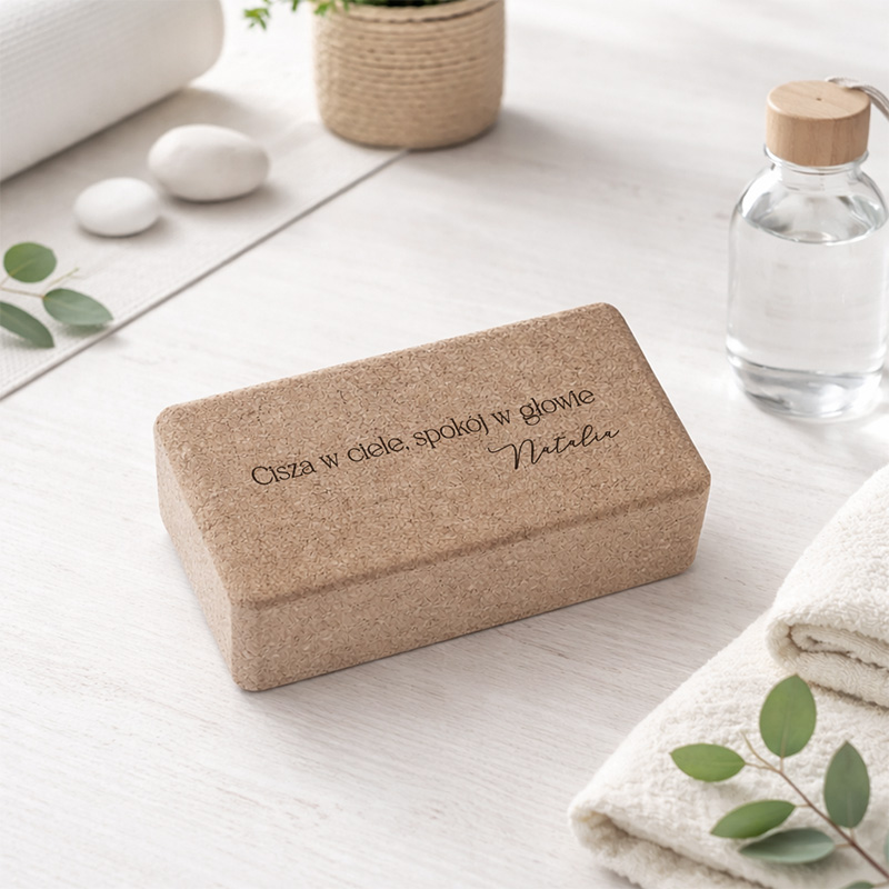 Słomkowe pudełko z napisem "Cisza w ciele, spokój w głowie" umieszczone na jasnym stole, w otoczeniu ręczników i botelki.