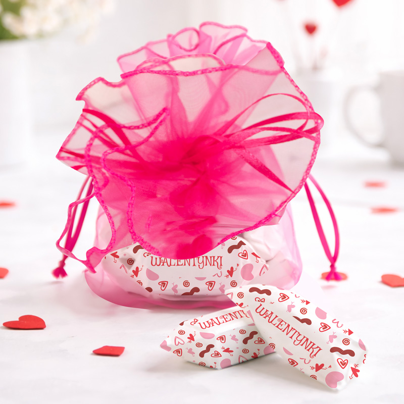 Różowa torba prezentowa z serduszkami, obok kilka małych czerwonych serc na białym tle.