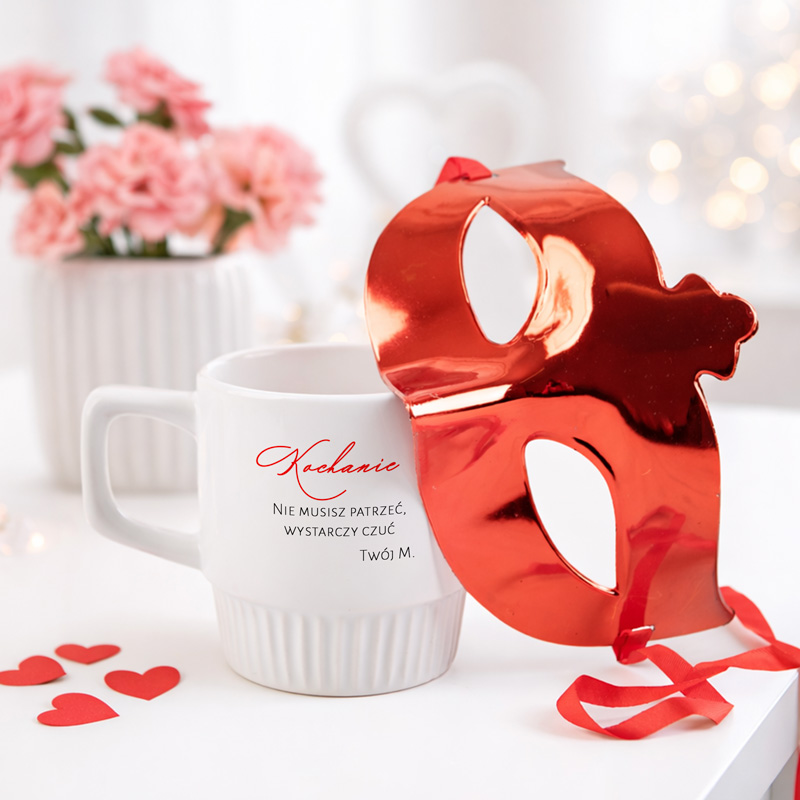 Czerwona maska leży obok białej filiżanki na tle różowych kwiatów i serduszek, z napisem „Nie musisz patrzeć, wystarczy czuć”.