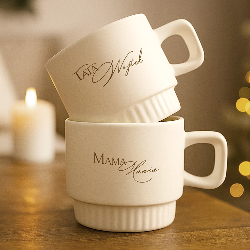 Dwa białe kubki ceramiczne z eleganckim napisem: "Tata Wojtek" na górnym i "Mama Hania" na dolnym.