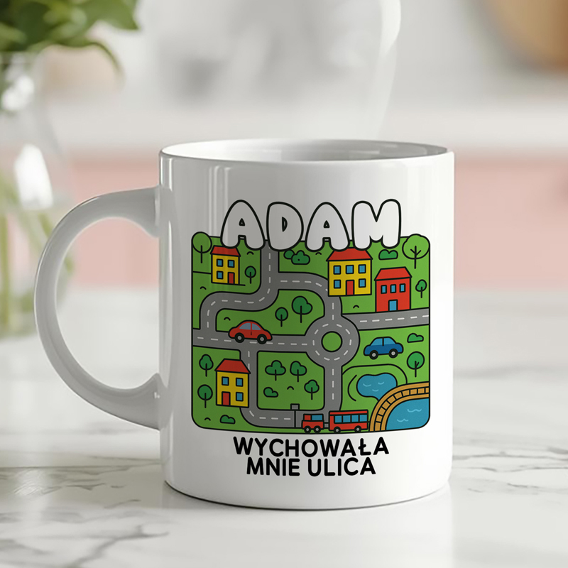 Kubek z grafiką przedstawiającą uproszczoną mapę z drogami, domami i pojazdami oraz napisem "ADAM WYCHOWAŁA MNIE ULICA".