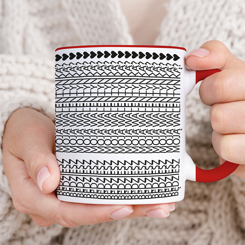 Kubek z białym wzorem w czarne linie na tle, trzymany przez osobę w swetrze.