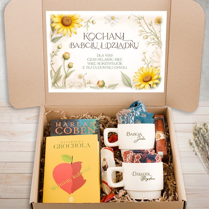 Wielka tektura z napisem "Kochani Babciu i Dziadku" z kwiatami, wewnątrz pudełka dwie białe filiżanki, książka, słodycze i różne dodatki.