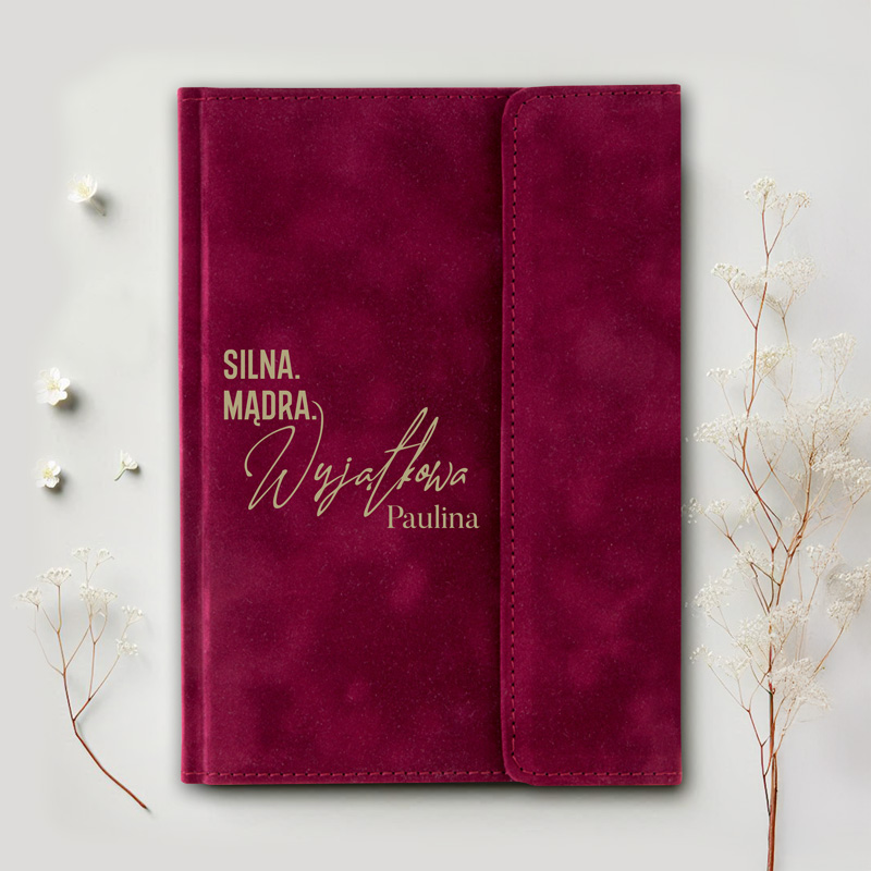 Ciemnofioletowy notes z napisem "SILNA. MĄDRA. Wyjątkowa Paulina" na okładce, otoczony delikatnymi kwiatami.