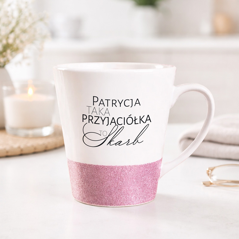 Filiżanka z napisem "Patrycja, taka przyjaciółka to skarb" oraz różowym, brokatowym wykończeniem. W tle widać świecę i tło kuchenne.