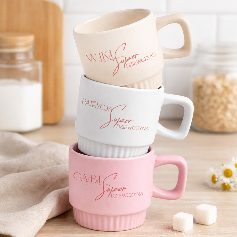 Trzy filiżanki w pastelowych kolorach: beżowa, szara i różowa, z napisem „Super Dziewczyna” w stylizowanej czcionce.