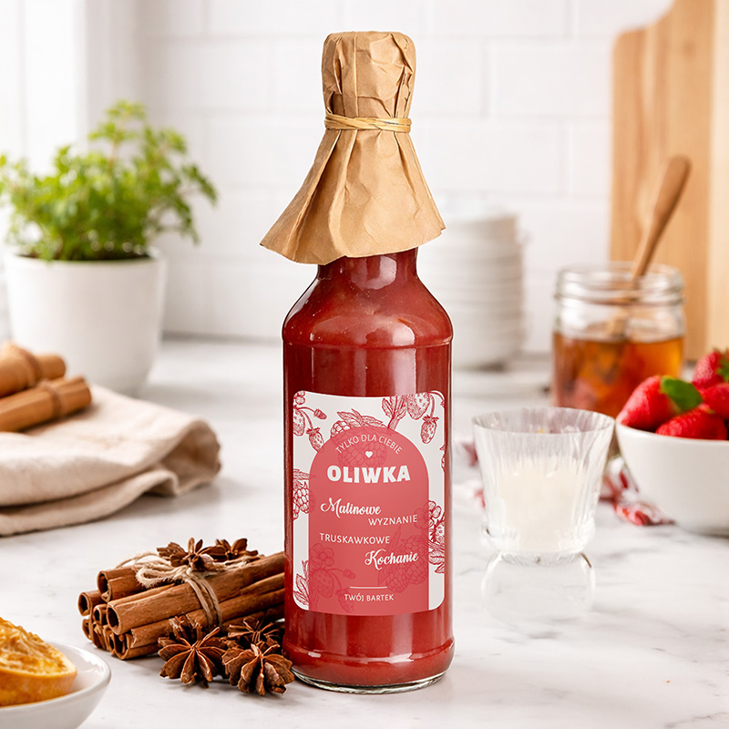 Słoik z truskawkowym syropem, zakręcony papierem, obok przyprawy i kieliszek, w tle świeże truskawki i słoik z dżemem.