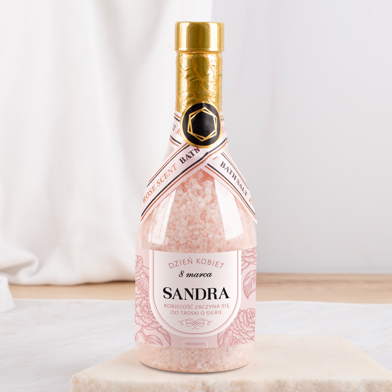 Butelka soli do kąpieli na Dzień Kobiet, ozdobiona różowym opakowaniem i etykietą z imieniem "Sandra".