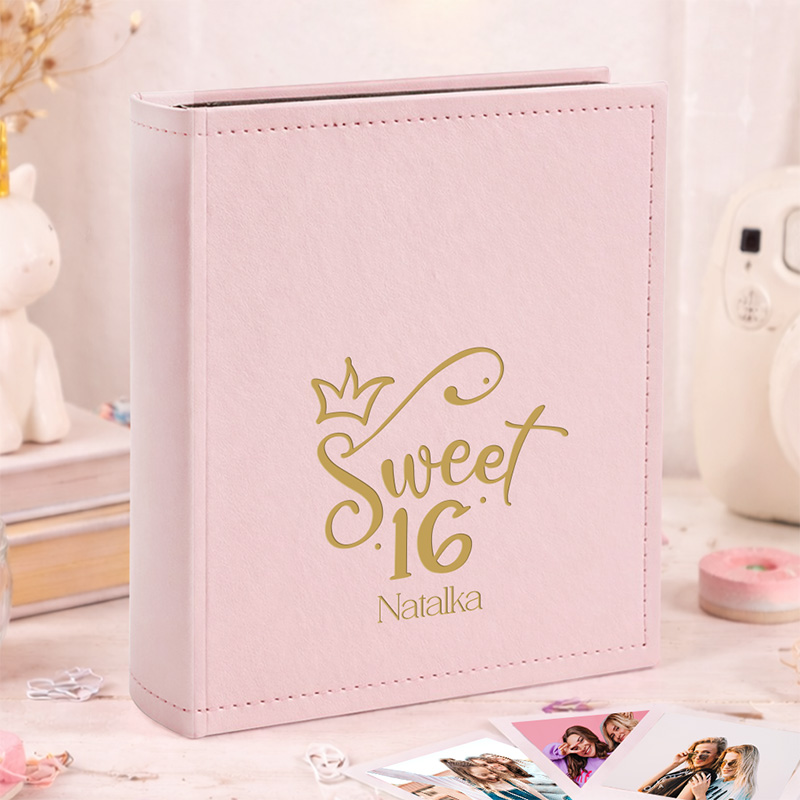 Różowy album na zdjęcia z napisem "Sweet 16 Natalka" i złotą koroną, otoczony dekoracjami i zdjęciami.