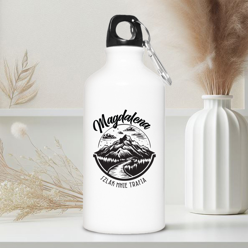 Biała butelka ze stalowym korkiem, z grafikiem górskim i napisem "Magdalena" oraz hasłem "Szlak mnie trafia".