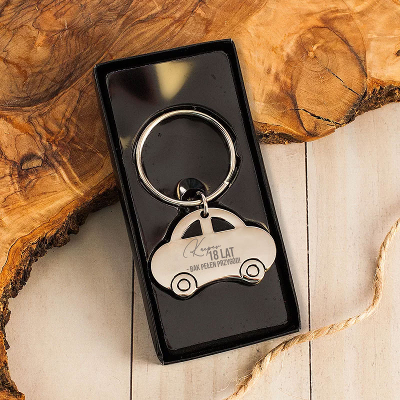 Breloczek w kształcie samochodu, zawieszony na metalowym kółku, z grawerem „18 LAT” w eleganckim opakowaniu.
