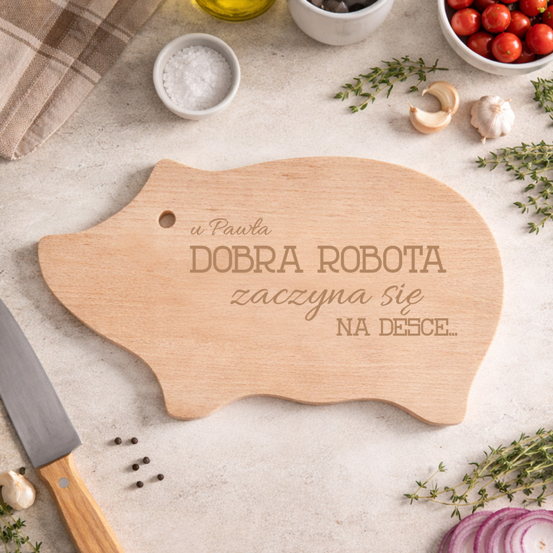 Deska do krojenia w kształcie świnki, na której widnieje napis: " DOBRA ROBOTA zaczyna się NA DESCE...".