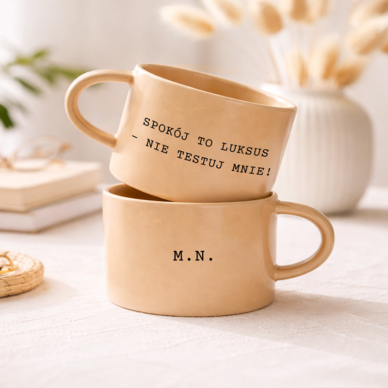 Dwa filiżanki w ciepłym odcieniu beżu, z napisem "SPOKOJ TO LUKSUS - NIE TESTUJ MNIE!" oraz inicjałami "M.N." na dolnej filiżance.