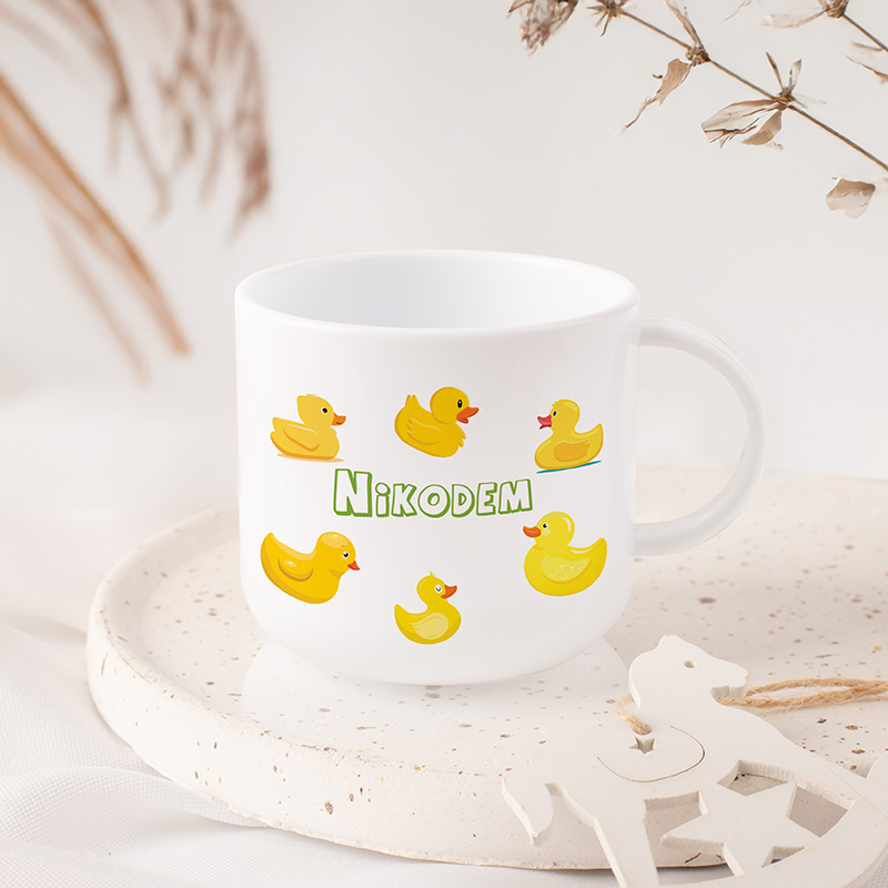 Biały kubek z żółtymi kaczuszkami i imieniem dziecka.