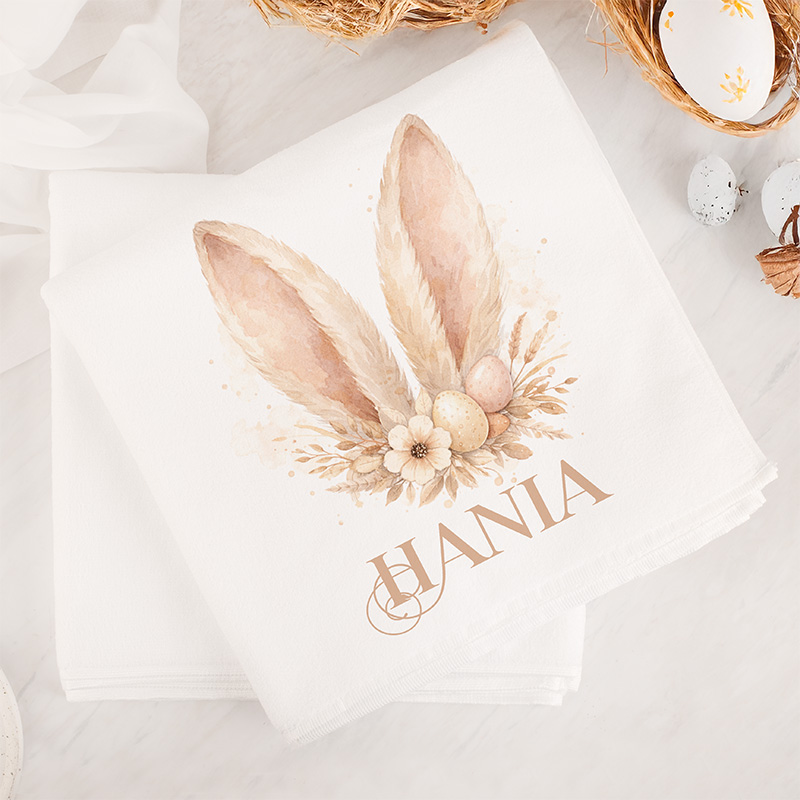 Ozdobny ręcznik z rysunkiem dużych uszu królika, kwiatami i jajkami, z imieniem w eleganckim stylu.