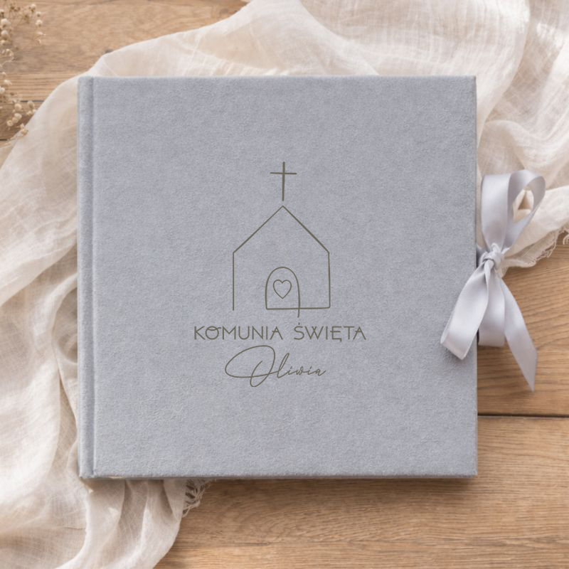 Szary album z wstążką, z widocznym napisem "Komunia Święta" i imieniem