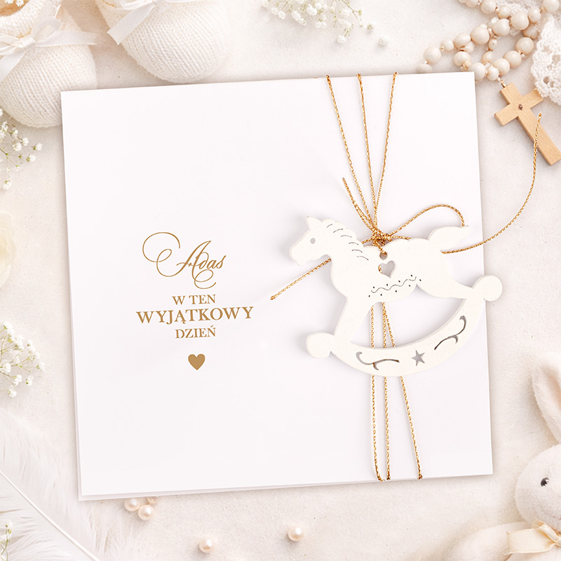 Biała kartka z złotym napisem "w ten wyjątkowy dzień" oraz zawieszonym konikiem na biegunach w eleganckim otoczeniu.