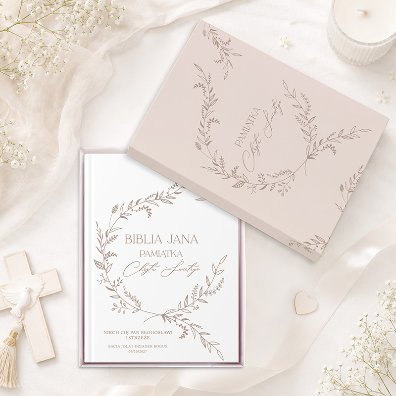 Elegancka Biblia z napisem "Pamiątka Chrztu Świętego" w ozdobnym opakowaniu, otoczona białymi kwiatami i drewnianym krzyżykiem.