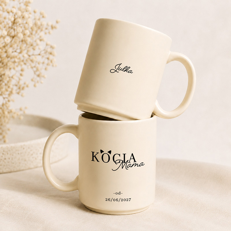 Dwa jasne kubki ceramiczne, jeden na drugim, z napisami: "Julia" i "KOCIA Mama", data "26/06/2027" na dolnym kubku.