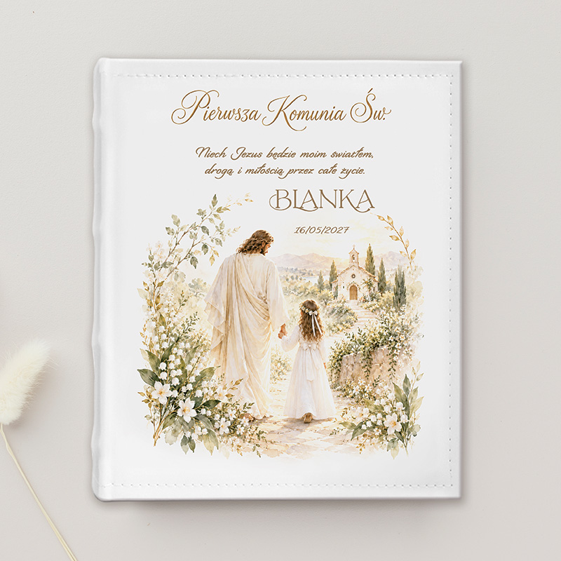 Elegancka, biała okładka albumu komunijnego z napisem "Pierwsza Komunia Święta". Ilustracja przedstawia Jezusa prowadzącego dziewczynkę w świętej scenerii.
