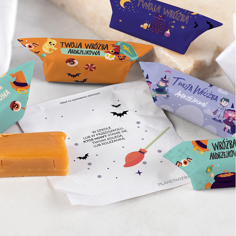 Różnokolorowe opakowania z wróżbami oraz karteczka z tekstem, w tematyce halloweenowej, leżące na jasnym tle.