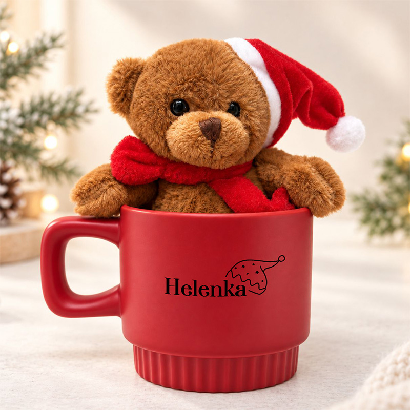 Miś w czerwonym kubku nosi świąteczną czapkę i szalik, z imieniem "Helenka" na kubku. Tło dekoracyjne z choinkami.